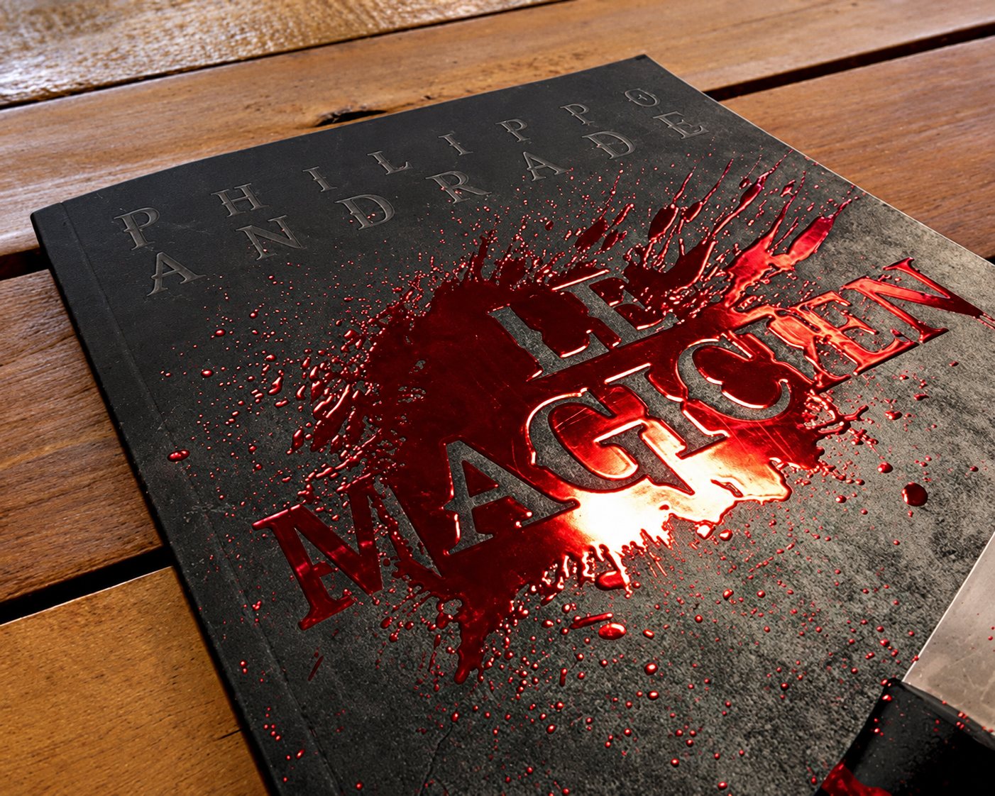 Livre à couverture noire avec éclaboussure rouge en vernis 3D et dorure sur une table en bois